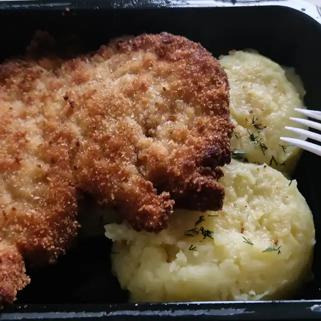 Duży kotlet schabowy z ziemniakami w pojemniku na wynos